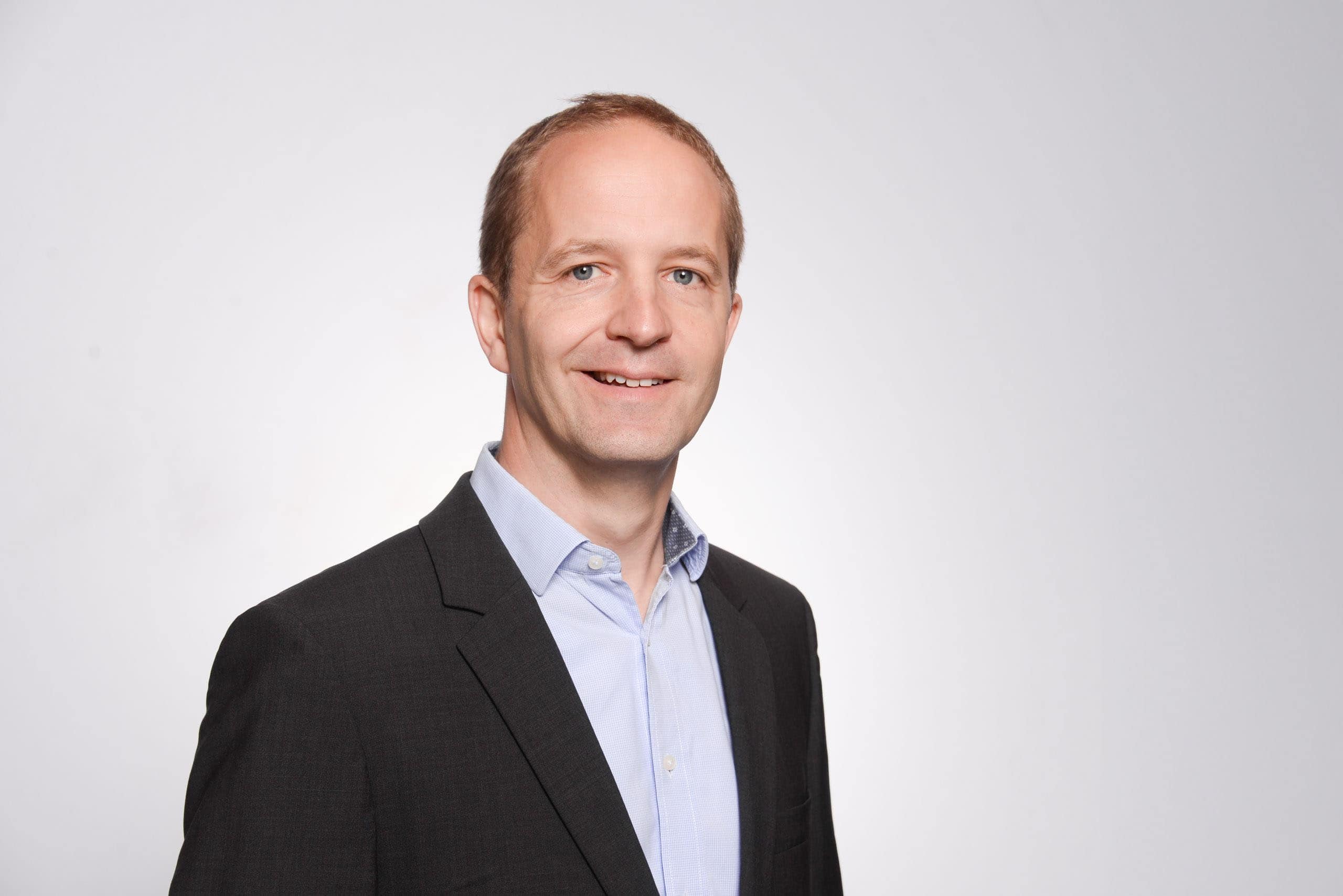 Headshot of a professional man in a suit, corporate portrait, business executive headshot for marketing and branding purposes, modern professional image for website or LinkedIn, clean grey background.